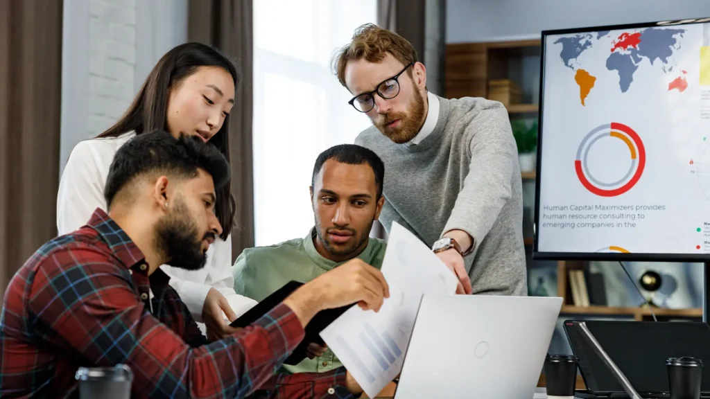 A diverse marketing team analyzing data dashboards and charts on a large screen to measure campaign performance and calculate marketing Return on Investment